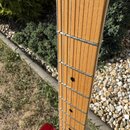 Detail krku elektrické kytary se světle hnědým javorovým hmatníkem. Na hmatníku jsou vidět kovové pražce a černé tečkové značky poloh. V horní části…