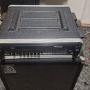 Černý basový zesilovač v transportním pouzdře umístěný na černém basovém kombu. Na předním panelu zesilovače je nápis Ampeg SVT-3 PRO. Na mřížce komb…