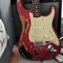 Elektrická kytara typu Stratocaster s červeným lakem a krčkem z tmavého dřeva. Lak na těle je výrazně opotřebovaný, s rozsáhlými odlakovanými místy a…