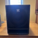 Černý reproduktor s mřížkou v horní části a otevřeným přehrádem v dolní části. Na mřížce je bílé logo s nápisem HK AUDIO. Povrch krycího materiálu vy…