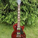 Červená elektrická kytara s tmavě hnědým hmatníkem a černým pickguardem. Na hlavě je bílý nápis Gibson a podpis Les Paul. Nástroj má dva humbuckery,…