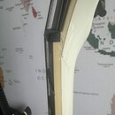 Detailní pohled na hranu bílého nástroje s černým plastovým lemováním. V místě spoje je viditelné výrazné poškození v podobě praskliny a odloupaného…