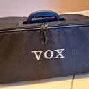 Černý textilní softcase s rukojetí. Na přední straně je bílý nápis VOX. Na horní části rukojeti je modrý nápis VOX. Povrch textilie vykazuje mírné op…
