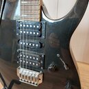 Černá elektrická kytara s třemi snímači (dvě humbuckery a jeden singl). Nástroj má chromovaný most s pružinami a dva ovládací knofíky s přepínačem. P…