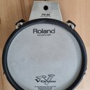 Kruhový elektronický trigger pad v šedé a černé barvě s kovovým uchytem. Na horní části je nápis PD-85 DUAL TRIGGER PAD a na membráně logo Roland s d…
