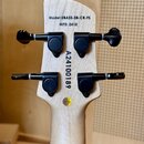 Zadní strana hlavy světlého dřevěného nástroje se čtyřmi černými ladicími kolíky. V horní části je nápis Model:UBASS-SB-CR-FS a MFD: 2410. Podstřední…