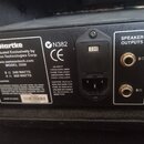 Zadní strana černého zesilovače s několika štítky a konektory. Na levém štítku je nápis Hartke, Distributed Exclusively by Samson Technologies Corp.,…