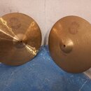 Dva mosazné činely s jemným rýhováním povrchu. Oba mají v horní části vyryté logo SOUND FORMULA. Levý činel má nápis Medium Heavy HiHat Bottom 14, pr…