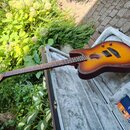 Akustická kytara s cutawayem v červenohnědém sunburst provedení, položená v otevřeném šedém tvrdém pouzdře. Na hmatníku jsou vidět pražce a na těle č…