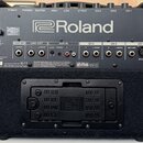 Zadní strana černého komba s nápisem Roland. Na panelu jsou vidět ovládací prvky, vstupy a výstupy s popisky: POWER, PHONES, MASTER, HIGH, LOW, EFFEC…