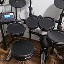 Elektronická bicí souprava v černé barvě s černými pady a činely. Na několika padych je viditelný nápis ARLSBROG, stejný nápis je i na pedálech. Souč…