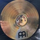 Zlatavý kovový činel s kovaným povrchem a vyvýšeným středem. V dolní části je černé logo ve tvaru stylizovaného písmene B a nápis MEINL. Povrch vykaz…