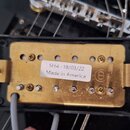 Fotografie znázorňuje elektrokitarový snímač s mosazným krytem a černým plastovým rámečkem. Na krytu je bílá nálepka s nápisem „SH4 - 18/03/22 Made i…
