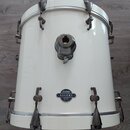 Bílý buben s kovovými obručemi a mechanismy. Na přední straně je oválný štítek s nápisy SONOR, ASCENT a pod nimi menším písmem BEECH SHELL / MADE IN…