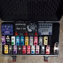 V otevřeném černém kufru s pěnovou výplní je uspořádán pedalboard s řadou efektů a malým zesilovačem. V horní části je modrý pedál JOYO CHOPPER-Z, če…