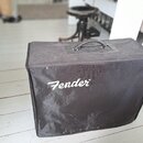 Černý textilní kryt na hudební zařízení s rukojetí v horní části. Na přední straně je bílý nápis Fender®. Povrch materiálu vykazuje známky opotřebení…