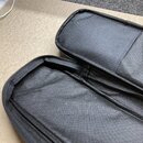 Otevřený černý textilní obal z syntetického materiálu s jemnou texturou. Vnitřní prostor je prázdný a v horní části se nachází přišitá kapsa. Na povr…