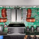 Fotografie zachycuje vnitřek elektronického zařízení s zelenou základní deskou. Jsou zde vidět čtyři velké měděné cívky, dva hliníkové chladiče a čer…