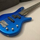 Modrá elektrická basová kytara s kovovými potenciometry a mostem. Nástroj má dva snímače v provedení humbuckerů a světlý hmatník. Na těle ani na hlav…