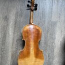 Fotografie znázorňuje zadní stranu smyčcového nástroje, pravděpodobně houslí, s hnědým lakovaným povrchem. Nástroj má dřevěné tělo, hmatník a kolíčky…