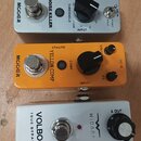 Tři efektové pedály v řadě. Horní stříbrný pedal má nápisy NOISE KILLER, MCGER a ovládací prvky THRESHOLD s hodnotami -70, -30, -20, -10, 0, +10dB a…