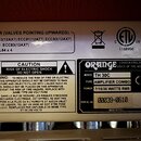 Detailní záběr na zadní štítky kytarového komba. Na černém štítku je bílé logo ORANGE a nápisy LONDON ENGLAND, VOICE OF THE WORLD, MODEL TH 30C, TYPE…