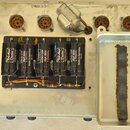 Fotografie zachycuje vnitřní elektroniku zařízení s několika elektrolytickými kondenzátory. Na černých válcích jsou bílé nápisy „Tube Amp Doctor“, „A…