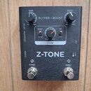Černý efekt pedál s nápisem Z-TONE. Na pravé straně jsou dva otočné knoflíky s popisky GAIN a BOOST, tři přepínače s označením PASSIVE/ACTIVE, SHARP/…