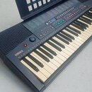 Černý elektronický klávesový nástroj značky YAMAHA. Na levé straně je vidět logo YAMAHA, červené tlačítko a ovládací prvky s nápisy MASTER VOLUME a D…