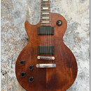 Elektrická kytara s hnědým dřevěným povrchem a dvěma černými humbuckery. Nástroj má čtyři černé oválné knofíky, stříbrný kobylník a stop-bar strunovn…