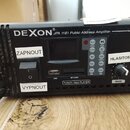 Černý zesilovač s nápisem DEXON JPA 1181 Public Address Amplifier. Přístroj obsahuje vestavěný modul s nápisem TUNER / Mp3 PLAYER, sloty USB a SD CAR…