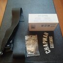 Na černém kufru s nápisem CHAPMAN GUITARS je položen černý popruh a bílá krabička s nápisem TELE PICKUPS a logem Fralin. Na krabičce jsou zaškrtnuté…
