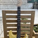 Světle žlutá elektrická kytara s bílým pickguardem a hnedým hmatníkem. Na hlavě krku je viditelné logo "Squier". Nástroj vykazuje známky běžného použ…
