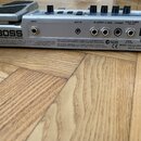 Zadní strana stříbrného efektového pedálu s nápisy BOSS a ME-20 GUITAR MULTIPLE EFFECTS. Jsou zde vidět konektory INPUT, AUX IN, R-OUTPUT-L/MONO, PHO…