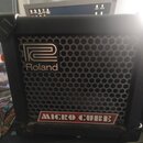 Černý kytarový kombo zesilovač s kovovou mřížkou reproduktoru. Na přední straně je umístěno logo Roland a nápis MICRO CUBE v červeném rámečku. Povrch…