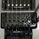 Detail elektrické kytary s černým humbuckerem, který nese nápis DUNCAN DESIGNED. Pod snímačem je černý tremolo systém s nápisem Floyd Rose Special. V…