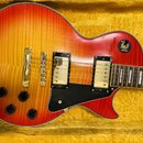 Elektrická kytara s trupem v červeno-žlutém sunburst provedení a viditnou strukturou dřeva. Nástroj má dva humbuckery s krémovými rámečky, černý plec…