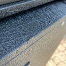 Detailní záběr na černý povrch přístroje potažený texturovaným vinylem. V horní části je viditelný štítek s anglickým a francouzským textem, který ob…