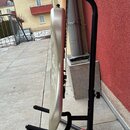Stříbrná elektrická kytara umístěná v černém kovovém stojanu. Kytara je zobrazená z profilu, povrch je hladký a lesklý. Na nástroji nejsou viditelná…