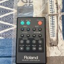 Černý dálkový ovladač značky Roland s nápisem REMOTE CONTROLLER. Obsahuje několik tlačítek s popisky ALL, MUTE, POWER, PART, INST, LEVEL, REVERB, SON…