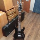 Černá elektrická kytara s špičatou hlavou a dvěma humbuckery, umístěná na stojanu. Na hlavě je bílé logo Ltd. Kytara má tmavý hmatník s bílými poloho…