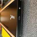 Černý elektronický přístroj s dřevěným rámem. Na horní části je bílý nápis „JPlay“. Na boční hraně jsou vidět USB-C port, malá kontrolka a dva kulaté…