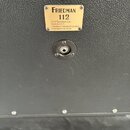 Detail zadní strany černého kytarového boxu s texturovaným povrchem. Na zlatém štítku je nápis FRIEDMAN 112, pod ním text 1x12" Extension Cab, Made i…