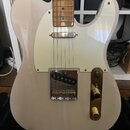 Světle béžová elektrická kytara typu Telecaster s bílým pickguardem a hnedým hmatníkem. Na kovovém krytu snímače je viditelný nápis Fender. Nástroj m…