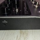 Černý efektový pedál s kovovým povrchem. Na přední hraně je umístěn vstup pro sluchátka s nápisem PHONES a ikonou sluchátek. Na horní části jsou vidě…