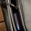 Detailní záběr na černý textilní obal s kovovým zipem. Na modrém štítku je bílý nápis pedaltrain. Povrch materiálu vykazuje běžné známky používání.