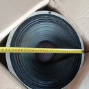 Fotografie znázorňuje velký černý reproduktor v kartonové krabici. Přes membránu je přeložen žlutýv metr, který ukazuje rozměr přibližně 34 cm. Na za…