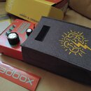 Červený efekt pedál s nápisy „dreadbox KOMO REBI“. Na zařízení jsou tři kovové přepínače, dva černé otočné knoflíky a jeden stříbrný knoflík. Vedle p…