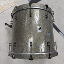 Zlatavě štítek s nápisem jelen DRUMS a logem v podobě stylizovaného kruhu. Jedná se o buben s povrchem v šedé glitrové barvě a chromovaným kováním. P…