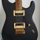 Elektrická kytara s matně černým korpusem a hnedým hmatníkem. Nástroj má dva snímače typu humbucker a hardware v zlatém provedení. Na kobylce je vidi…